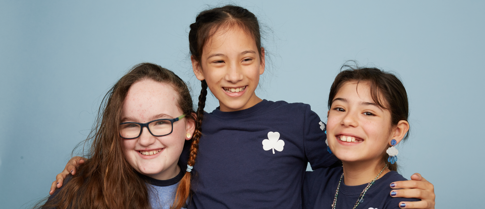 Two Guide-aged girls in uniforms huging in a blue background