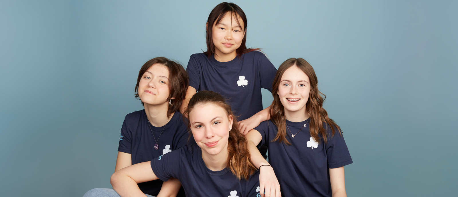 Four Ranger-aged girls in uniforms smiling in a blue background